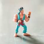 A small toy action figure with a cyan karate outfit and red belt posed ready to fight
